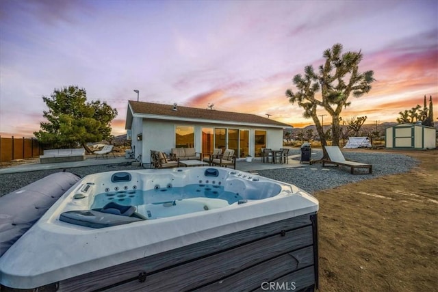 pool at dusk with a hot tub, a patio area, and a storage unit