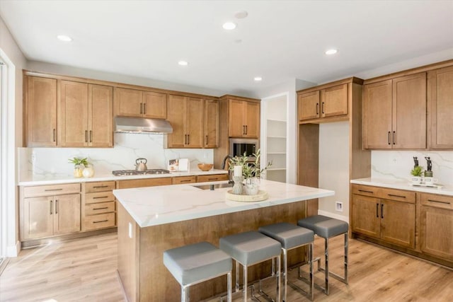 kitchen featuring an island with sink, sink, a breakfast bar area, stainless steel gas cooktop, and light wood-type flooring