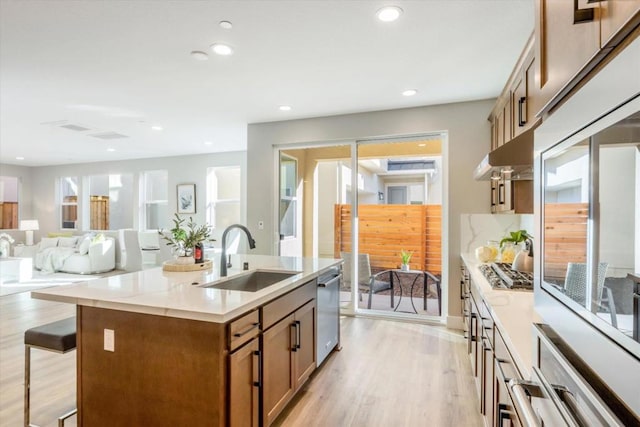 kitchen featuring sink, stainless steel appliances, an island with sink, a kitchen bar, and light wood-type flooring