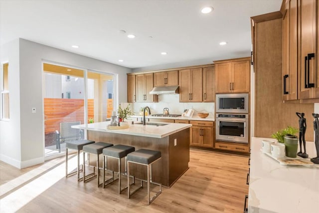 kitchen featuring sink, a breakfast bar area, light hardwood / wood-style flooring, stainless steel appliances, and a kitchen island with sink