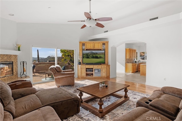 living room with ceiling fan, a high ceiling, a premium fireplace, and light hardwood / wood-style floors