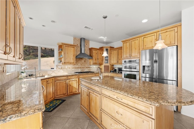 kitchen featuring wall chimney exhaust hood, a kitchen island with sink, decorative light fixtures, and appliances with stainless steel finishes