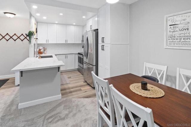 kitchen with light stone countertops, white cabinetry, sink, backsplash, and stainless steel refrigerator