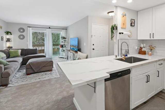 kitchen with white cabinetry, backsplash, light stone countertops, stainless steel dishwasher, and sink