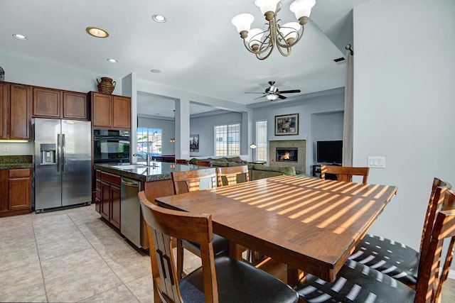 tiled dining space with a tiled fireplace, sink, and ceiling fan with notable chandelier