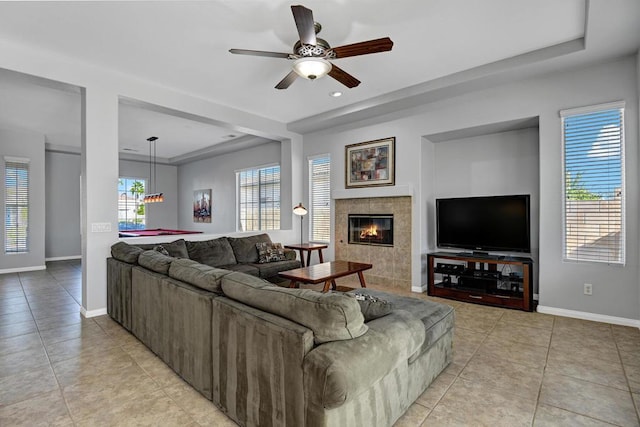 tiled living room with ceiling fan, a tray ceiling, a tile fireplace, and billiards