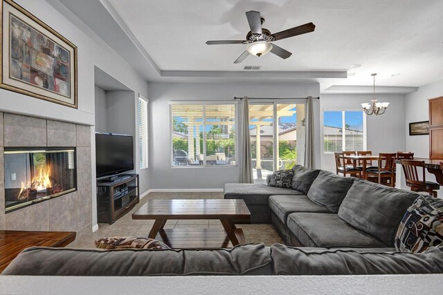 tiled living room featuring ceiling fan with notable chandelier, a wealth of natural light, and a tiled fireplace