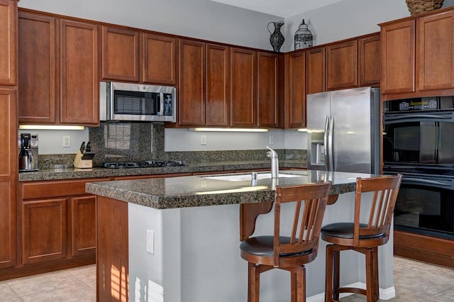 kitchen featuring light tile patterned floors, a kitchen bar, stainless steel appliances, a kitchen island with sink, and sink