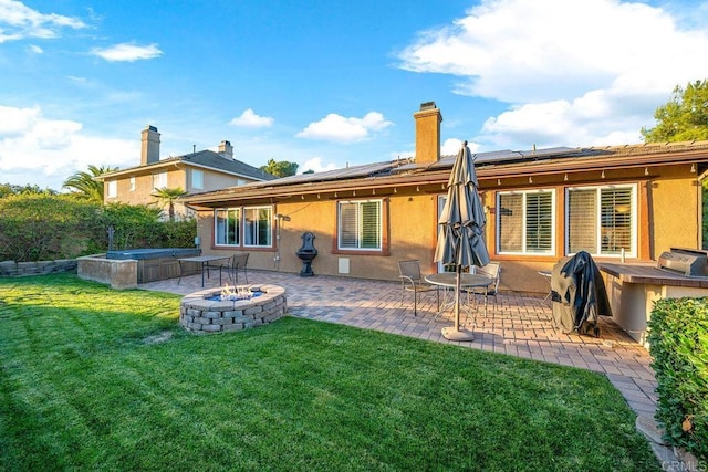 rear view of house featuring a hot tub, a lawn, solar panels, and a patio