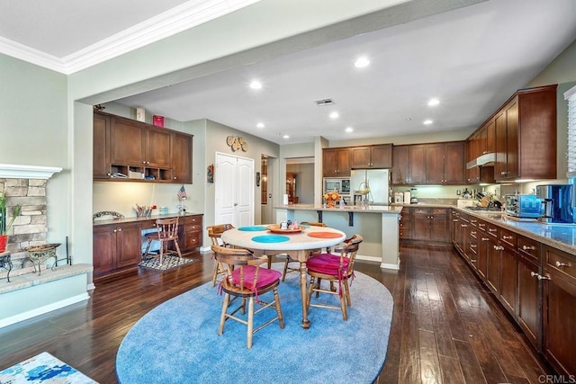 dining space featuring dark wood-type flooring, crown molding, and a stone fireplace