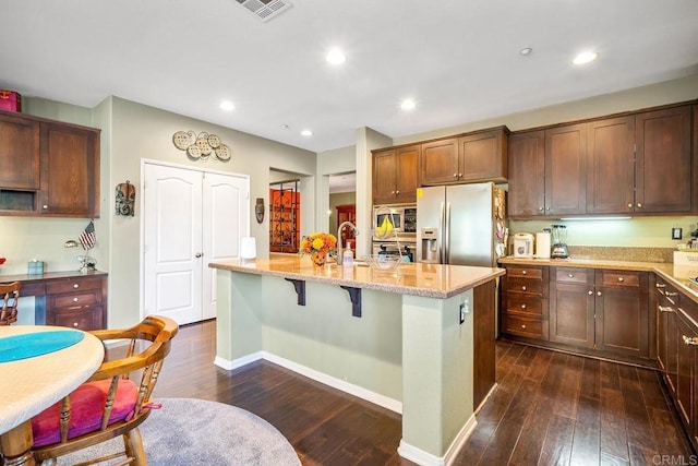 kitchen with a center island with sink, a breakfast bar area, appliances with stainless steel finishes, dark hardwood / wood-style floors, and light stone countertops