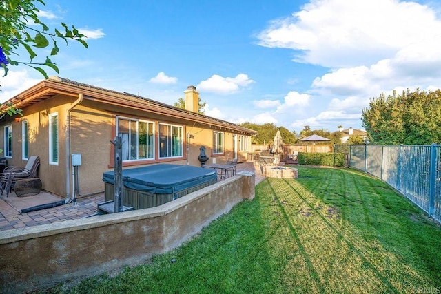 rear view of house with a hot tub, a lawn, and a patio