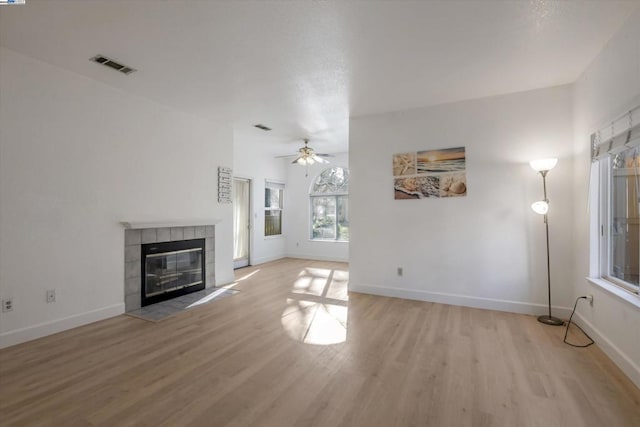 unfurnished living room featuring ceiling fan, light hardwood / wood-style flooring, and a tiled fireplace