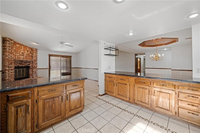 kitchen with a brick fireplace, pendant lighting, light tile patterned floors, dark stone counters, and ceiling fan with notable chandelier