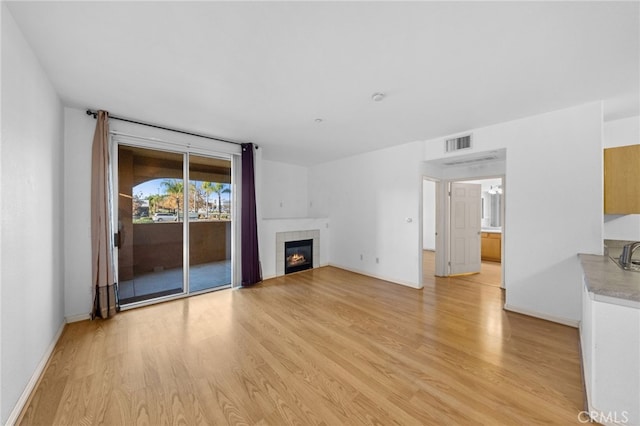 unfurnished living room featuring light wood-type flooring and a tiled fireplace