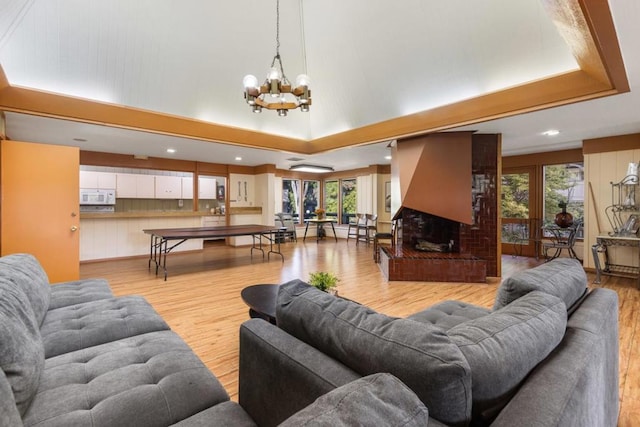 living room with a brick fireplace, light hardwood / wood-style flooring, a raised ceiling, and an inviting chandelier