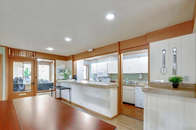 kitchen featuring white appliances, white cabinets, light hardwood / wood-style flooring, and kitchen peninsula