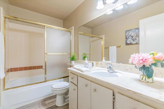 full bathroom featuring toilet, combined bath / shower with glass door, wood-type flooring, and vanity