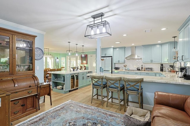 kitchen with beverage cooler, wall chimney exhaust hood, sink, hanging light fixtures, and stainless steel fridge