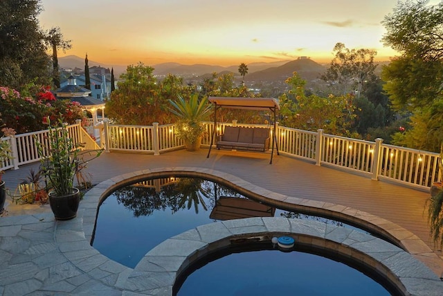 pool at dusk with a deck with mountain view and an outdoor hot tub