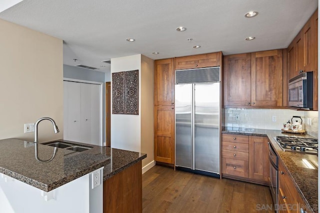 kitchen with kitchen peninsula, appliances with stainless steel finishes, dark hardwood / wood-style floors, dark stone counters, and sink