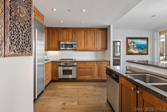 kitchen featuring backsplash, appliances with stainless steel finishes, dark stone countertops, and light hardwood / wood-style floors