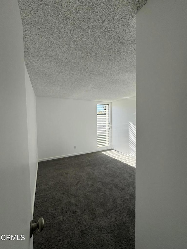 spare room with a textured ceiling and dark colored carpet