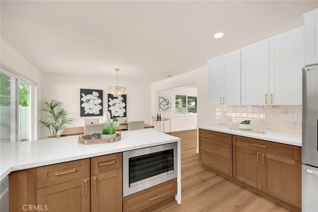 kitchen featuring white cabinetry, stainless steel appliances, an inviting chandelier, hanging light fixtures, and light hardwood / wood-style flooring