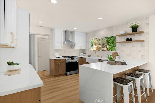 kitchen featuring kitchen peninsula, sink, white cabinetry, wall chimney exhaust hood, and stainless steel gas stove