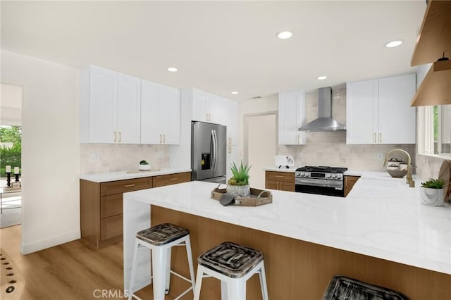 kitchen with stainless steel appliances, white cabinets, kitchen peninsula, and wall chimney range hood