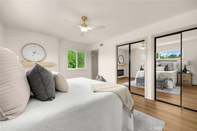 bedroom featuring ceiling fan, multiple closets, and light hardwood / wood-style floors