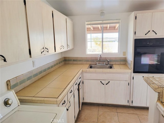 kitchen with oven, washer / dryer, tasteful backsplash, sink, and tile countertops