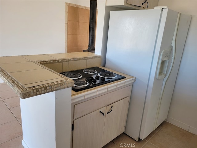 kitchen with kitchen peninsula, black electric stovetop, light tile patterned flooring, white fridge with ice dispenser, and tile countertops