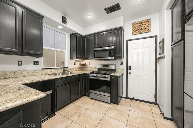 kitchen with appliances with stainless steel finishes, sink, light tile patterned floors, and light stone counters