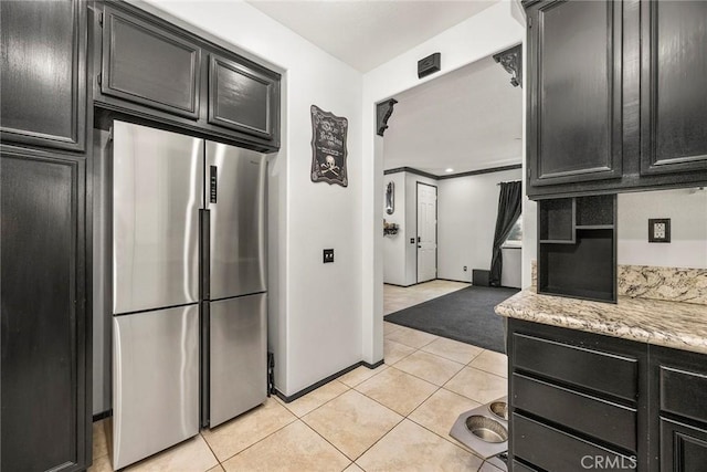 kitchen featuring light tile patterned floors, baseboards, dark cabinets, and stainless steel refrigerator