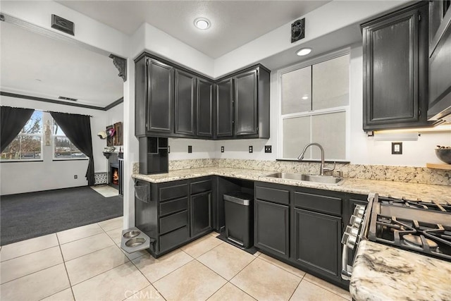 kitchen featuring a sink, light stone counters, a lit fireplace, light tile patterned floors, and light colored carpet