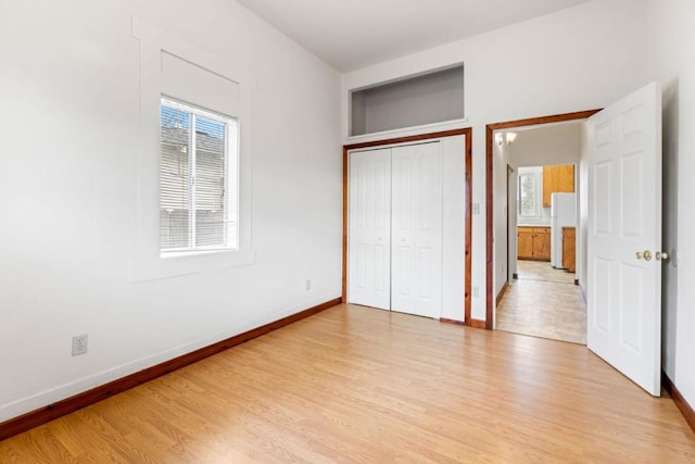 unfurnished bedroom featuring light hardwood / wood-style floors, white fridge, and a closet