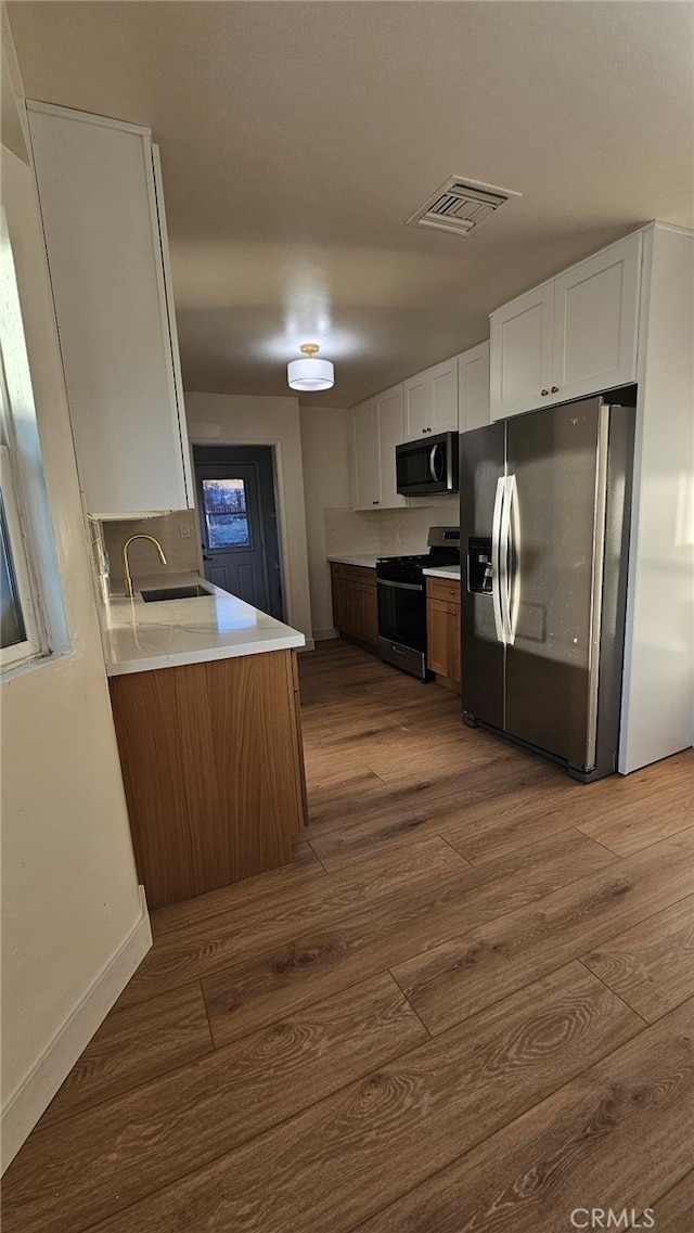 kitchen with appliances with stainless steel finishes, dark hardwood / wood-style flooring, white cabinets, and sink