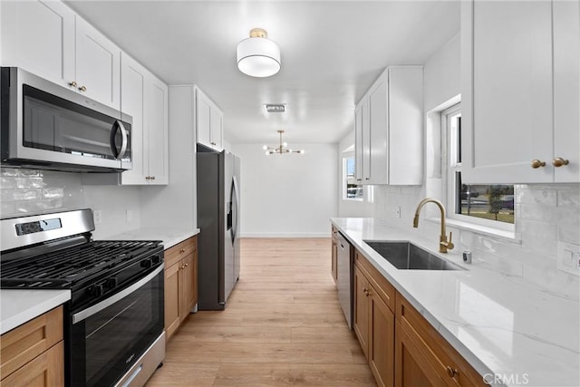 kitchen featuring a notable chandelier, sink, appliances with stainless steel finishes, white cabinets, and light stone counters