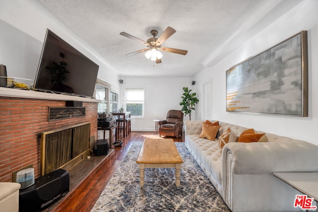 living room featuring dark wood-type flooring, a brick fireplace, a textured ceiling, and ceiling fan