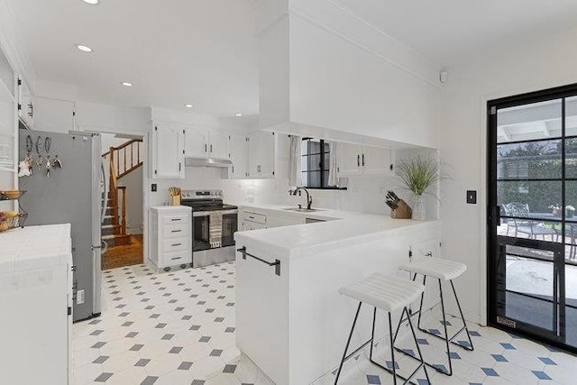 kitchen with white cabinets, white fridge, kitchen peninsula, a breakfast bar area, and electric range