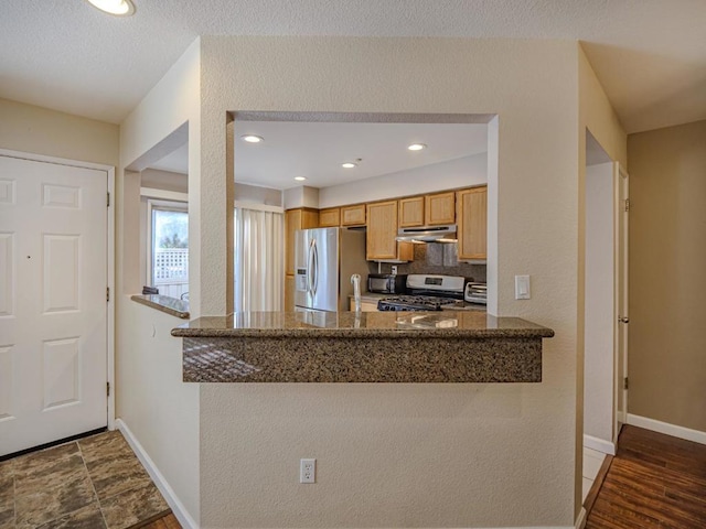 kitchen featuring kitchen peninsula, decorative backsplash, dark stone counters, and appliances with stainless steel finishes