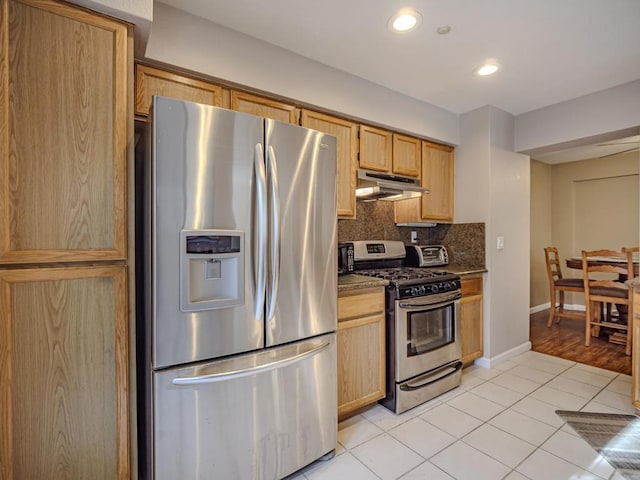 kitchen with appliances with stainless steel finishes, backsplash, light tile patterned floors, light brown cabinets, and dark stone countertops