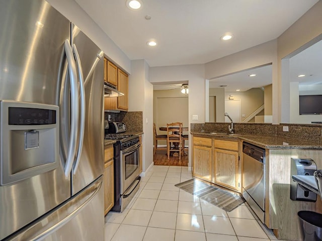 kitchen with appliances with stainless steel finishes, backsplash, sink, light tile patterned floors, and dark stone countertops