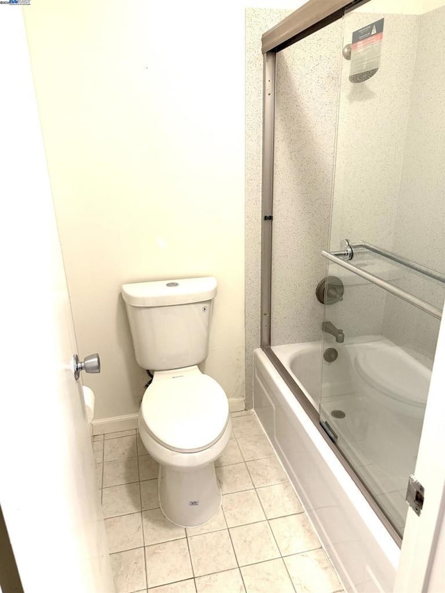 bathroom featuring toilet, bath / shower combo with glass door, and tile patterned floors