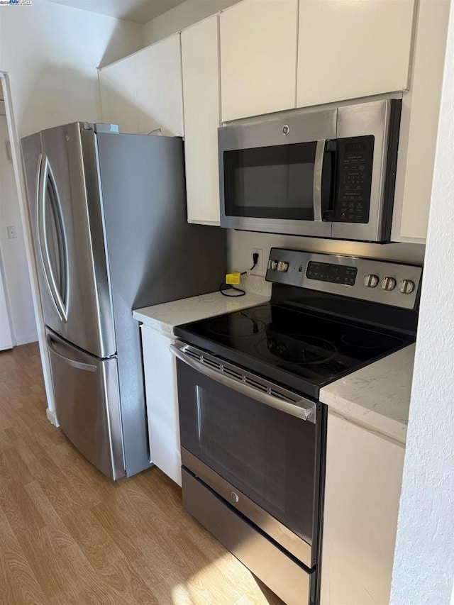 kitchen with white cabinets, light wood-type flooring, light stone countertops, and stainless steel appliances