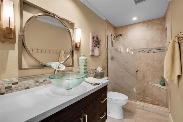 bathroom with vanity, backsplash, toilet, a tile shower, and crown molding