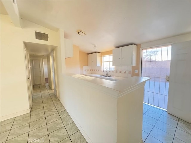 kitchen with white cabinetry, plenty of natural light, kitchen peninsula, vaulted ceiling, and light tile patterned floors