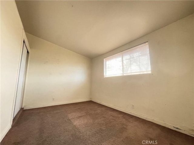 spare room featuring lofted ceiling and dark carpet