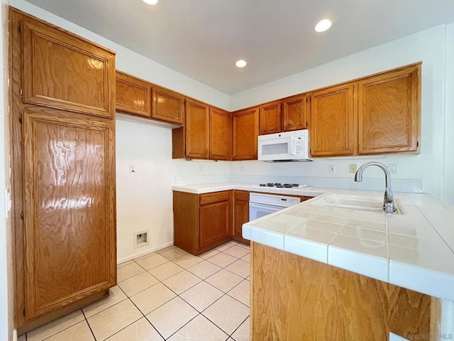 kitchen with tile countertops, kitchen peninsula, white appliances, light tile patterned flooring, and sink